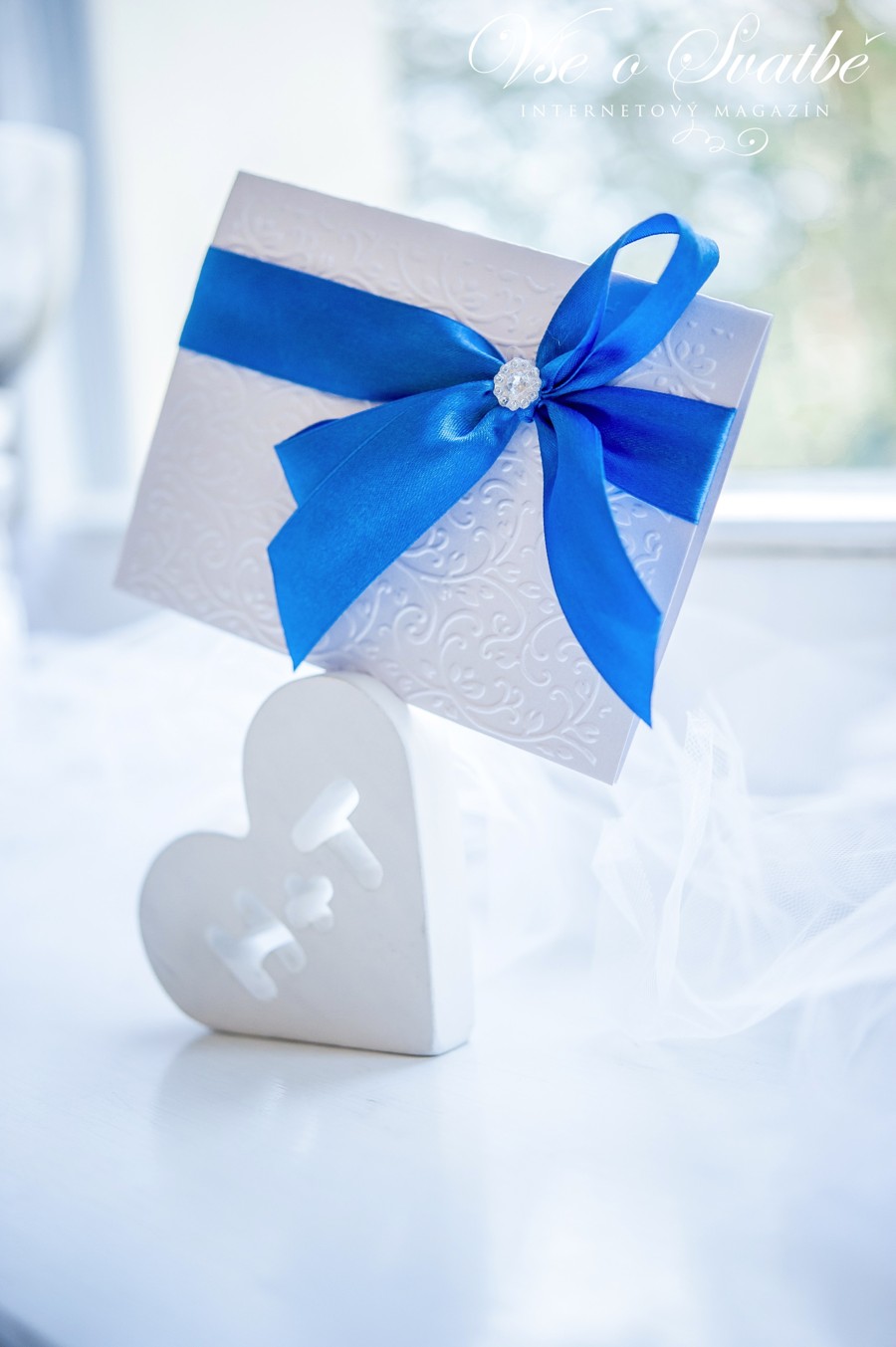 Bílá tlačená svatební pozvánka s modrou stuhou.
